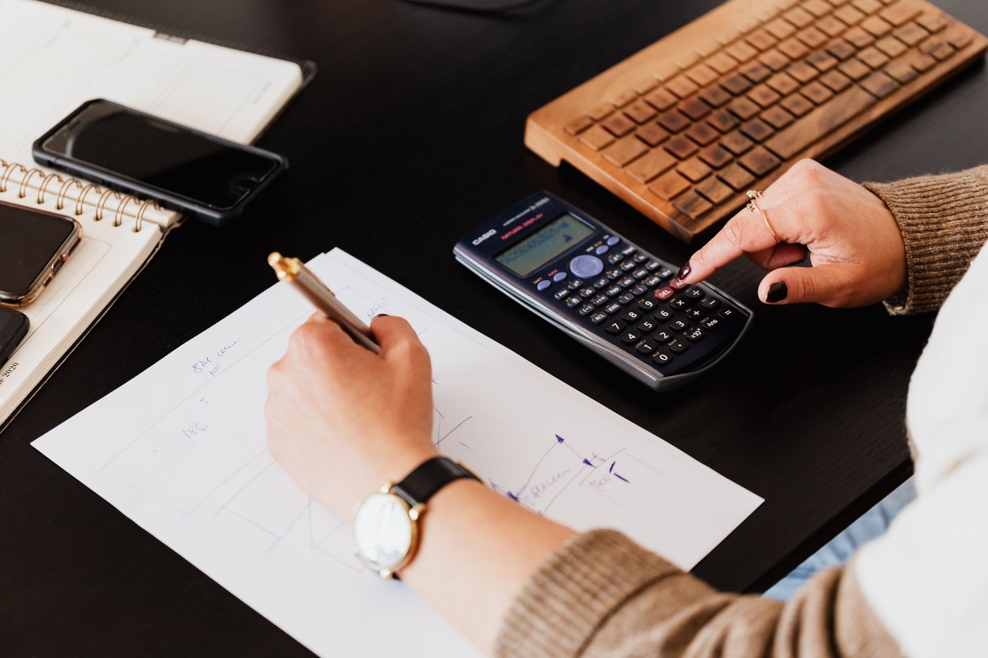 Hands using a calculator and writing notes at a desk